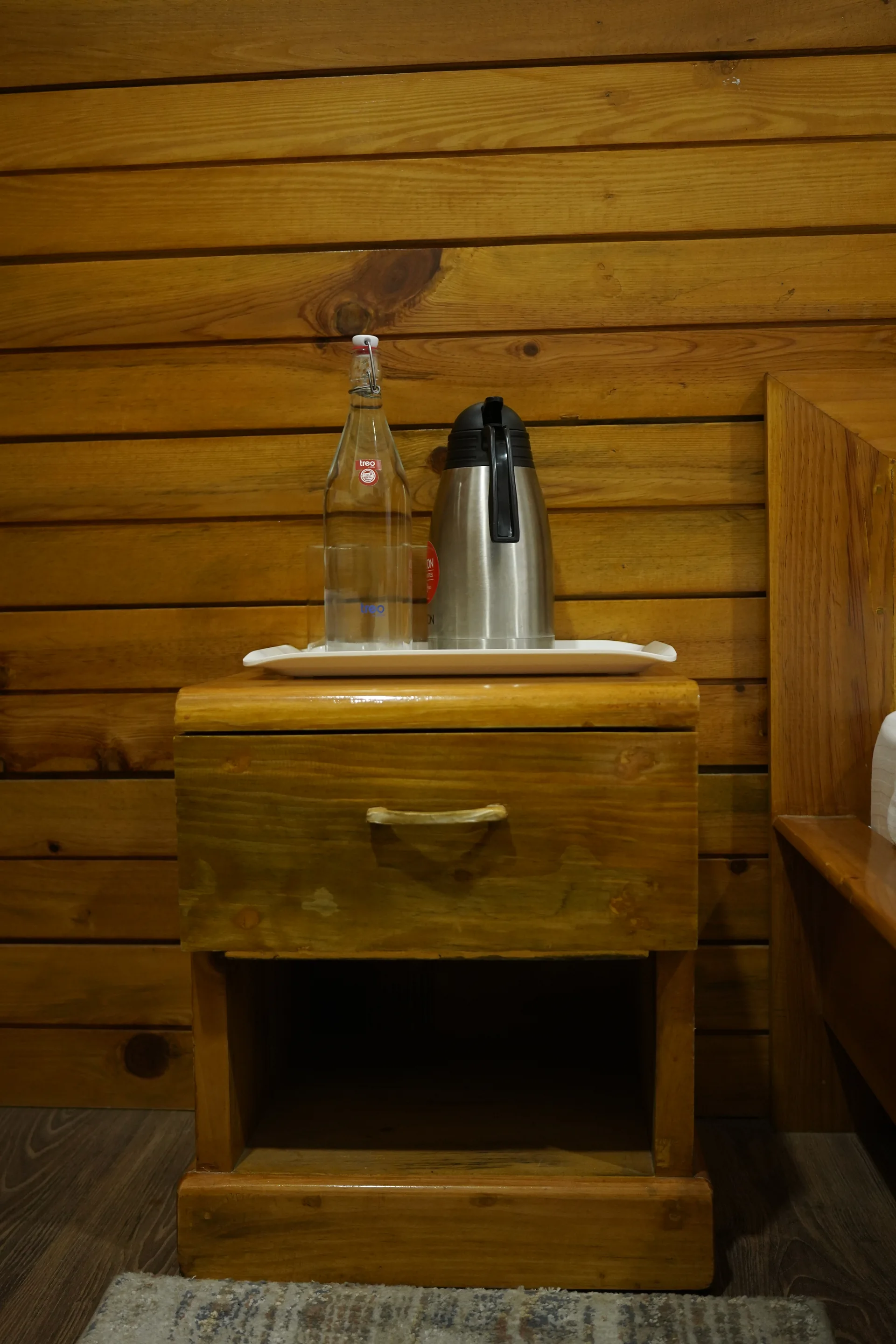 Wooden bedside table with thermos at Acorn Homestay